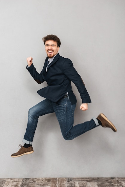 portrait of a handsome emotional young business man isolated over grey wall jumping.