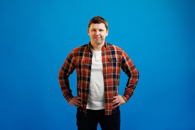 Portrait of handsome european man in shirt looking at camera standing on blue studio background