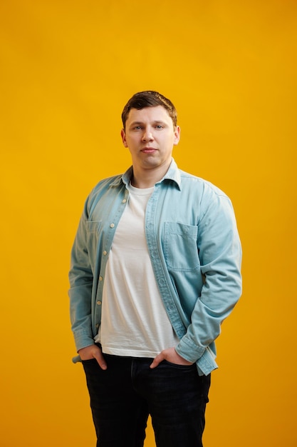 Portrait of handsome european man in shirt looking at camera standing on yellow studio background