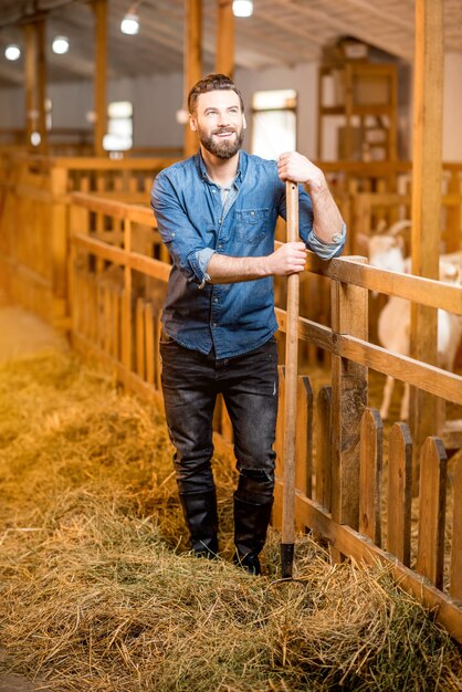 Portrait of a handsome farmer standing with fork at the goat barn. Natural milk production and farming