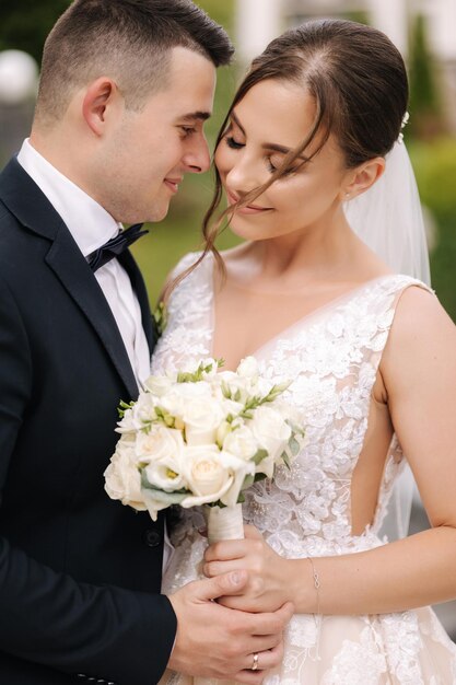 Portrait of handsome groom and gorgeous bride standing outdoor Bride hold bouquet Close up of man and woman hug each other