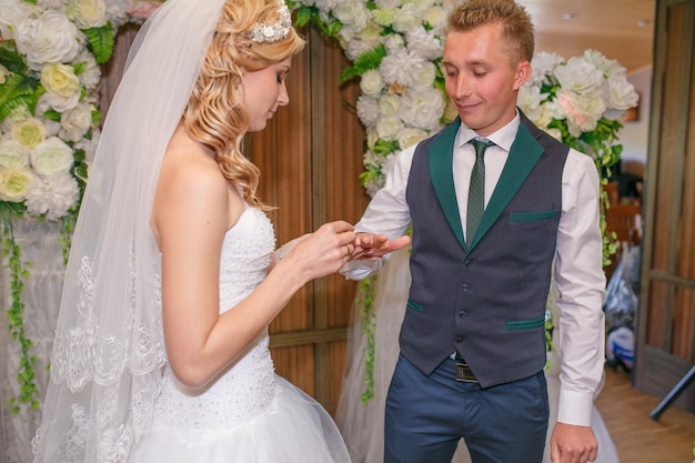 Portrait of handsome groom putting wedding ring on brides hand