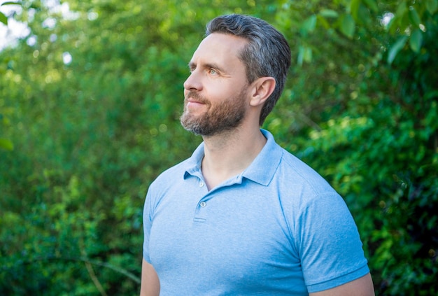 Portrait of handsome guy in blue tshirt looking aside natural background