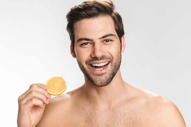 Портрет красивого полуобнаженного мужчины, улыбающегося и едящего лимон, изолированного на белом