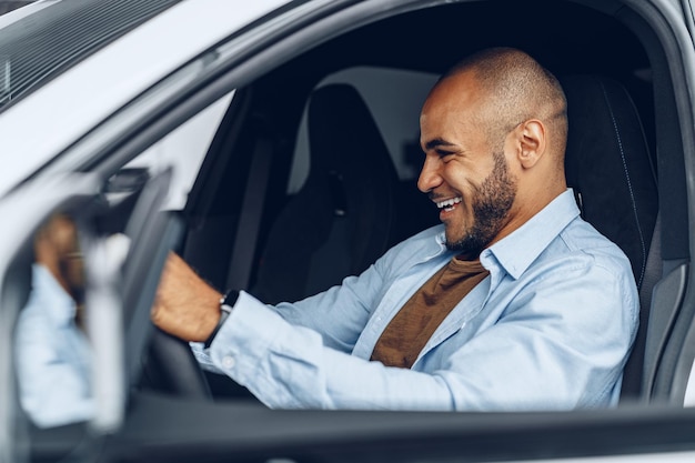 彼の新しく購入した車に座っているハンサムな幸せなアフリカ系アメリカ人の男の肖像画