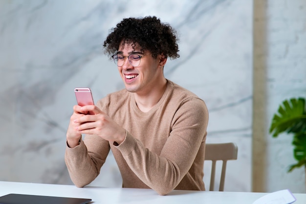 Portrait of handsome happy positive guy in glasses, young cheerful man is using gadget, looking at