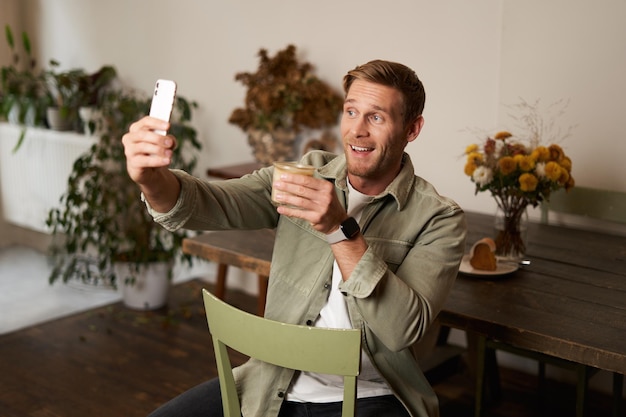 카페에서 셀피를 찍고 커피 한 잔과 함께 포즈를 취하는 잘생긴 행복한 젊은 남자의 초상화 비디오 채팅