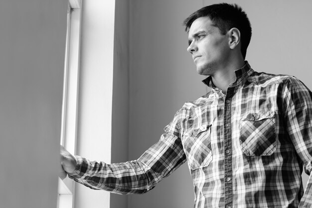 Portrait of handsome hipster man by the window at home indoors in black and white