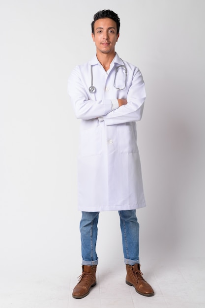 Portrait of handsome Hispanic man doctor against white wall