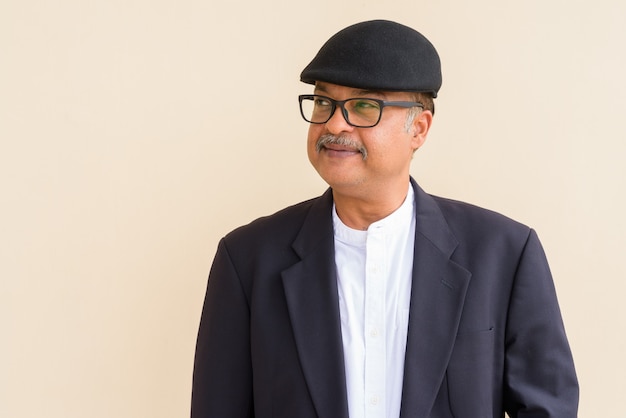 Portrait of handsome Indian businessman with mustache wearing hat against plain wall