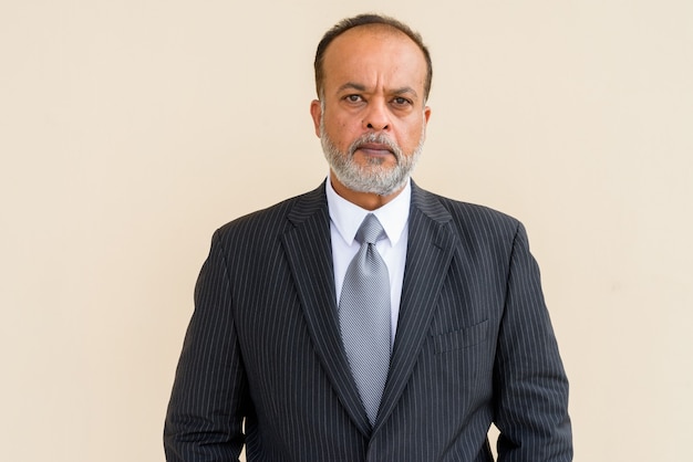 Portrait of handsome Indian man with gray beard against plain wall