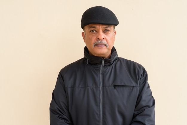 Portrait of handsome Indian man with mustache wearing hat against plain wall