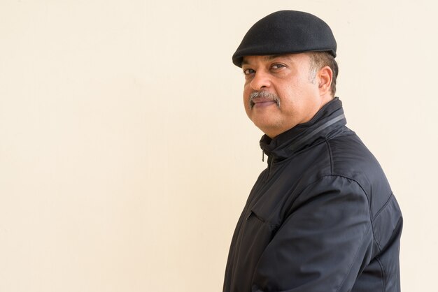 Portrait of handsome Indian man with mustache wearing hat against plain wall