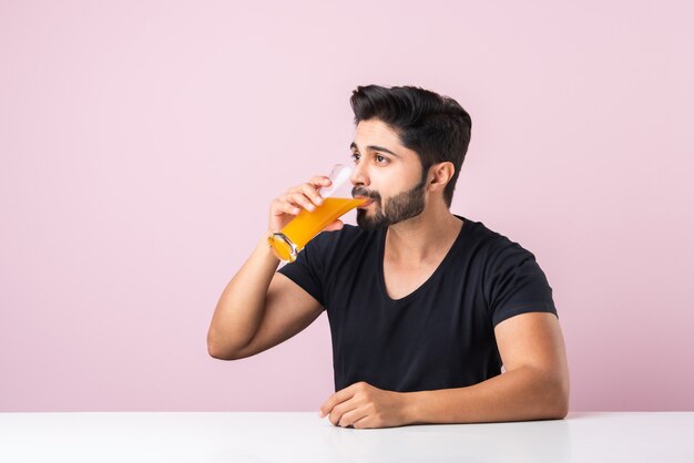 Portrait of a handsome Indian young man drinking orange juice in kitchen in the morning