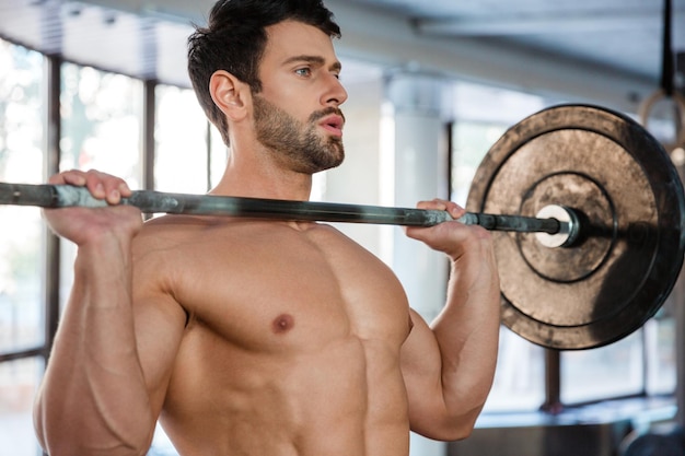 Portrait of a handsome male bodybuilder doing exercise with barbell in gym