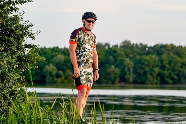 Portrait of a handsome male cyclist standing near river against a beautiful landscape with a lake Man looking away