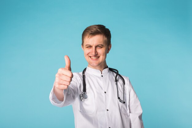 Portrait of handsome male doctor showing thumbs up over blue background