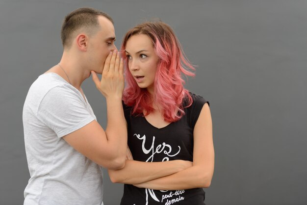 Portrait of handsome man and beautiful woman with pink hair as couple together and in love against gray wall outdoors