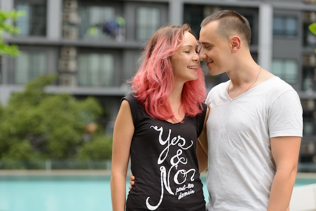 Portrait of handsome man and beautiful woman with pink hair as couple together in the swimming pool area outdoors