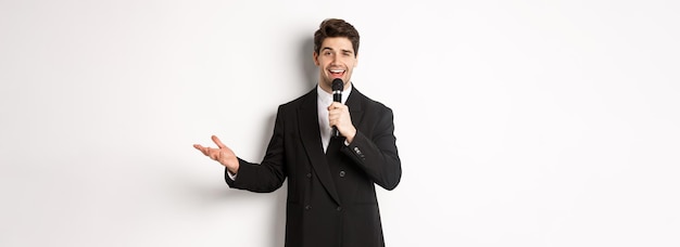 Foto ritratto di uomo bello in abito nero che canta una canzone tenendo il microfono e dando discorso in piedi