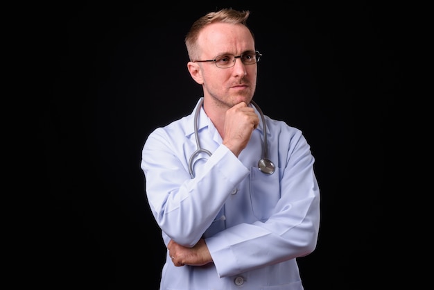 Portrait of handsome man doctor with blonde hair against black wall