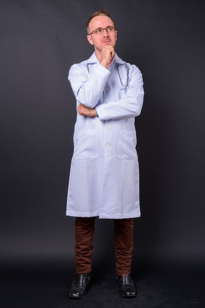 Portrait of handsome man doctor with blonde hair against black wall