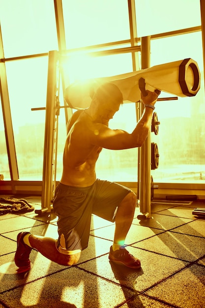 피트니스 체육관에서 햇빛 아래 현대적인 웨이트 기구로 운동하는 잘생긴 남자의 초상화