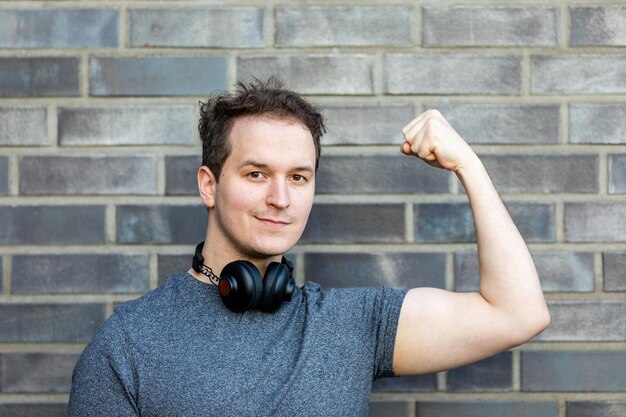 Photo portrait of handsome man flexing muscle against brick wall