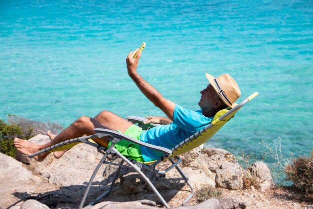 Foto ritratto di un bell'uomo sdraiato su una sdraio e che si fa un selfie durante le vacanze estive