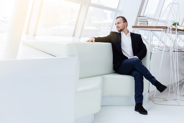 Portrait a handsome man sitting on the sofa in white modern interior. 