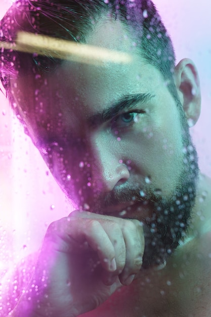 Portrait of handsome man through wet glass in neon light