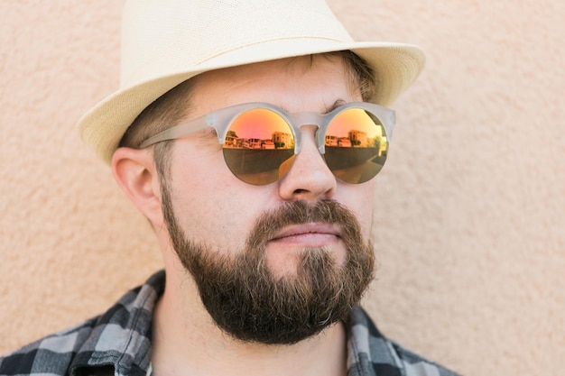 Portrait handsome man wearing summer hat and sunglasses and plaid shirt smiling happy near wall travel vacations and summer holiday concept