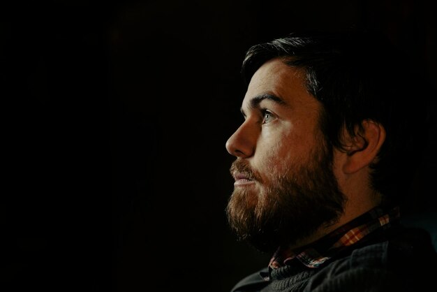 Portrait of a handsome man with a beard on a dark background in profile