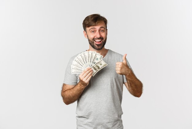 Portrait of handsome man with beard, showing thumbs-up and holding money