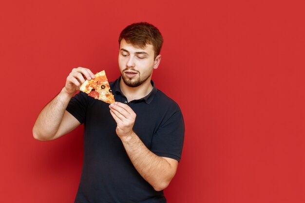 Portrait of handsome man with beard stands with piece of pizza in his hands