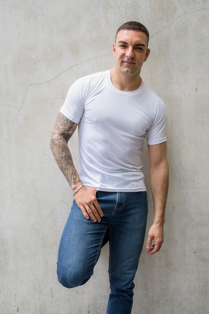 Portrait of handsome man with tattoos against concrete wall