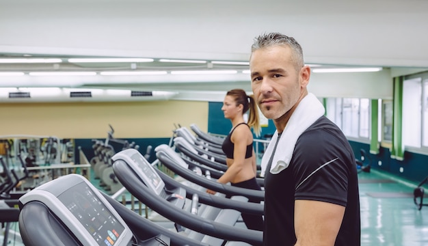 portrait of handsome man with towel in his neck training over a treadmill on fitness center