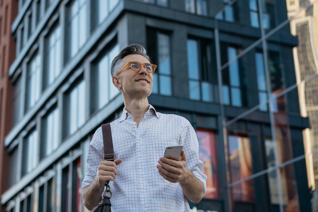 Portrait of handsome mature businessman holding messenger bag, wearing stylish eyeglasses