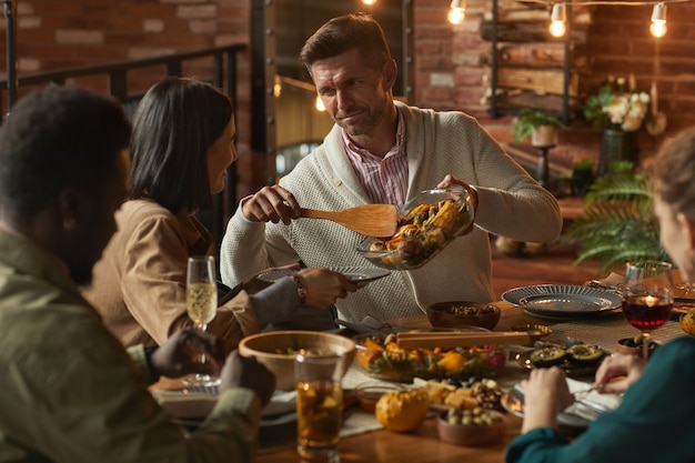 Portrait of handsome mature man serving food while hosting dinner party with friends and family, 