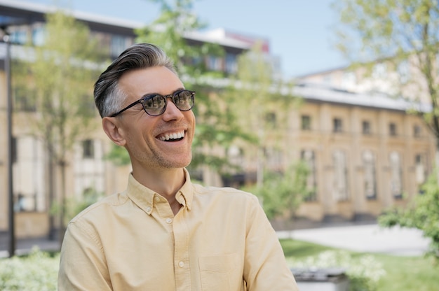 Portrait of handsome mature man wearing sunglasses, walking on the street, laughing.