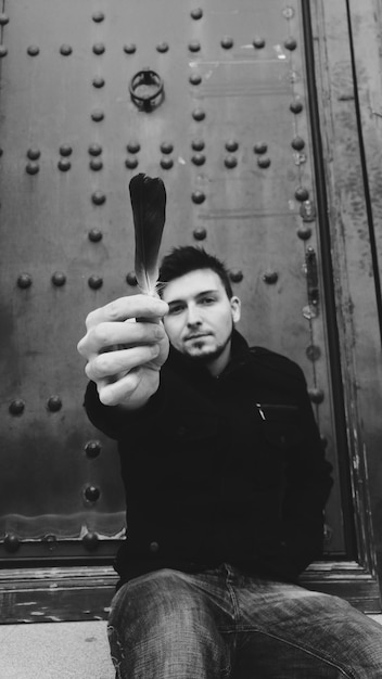 Photo portrait of handsome mid adult man holding feather against door