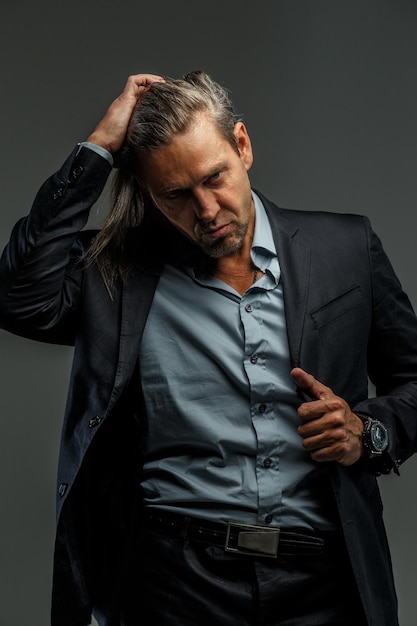 Portrait of handsome middle age long-haired stylish man in dark grey suit. Isolated on gray background.