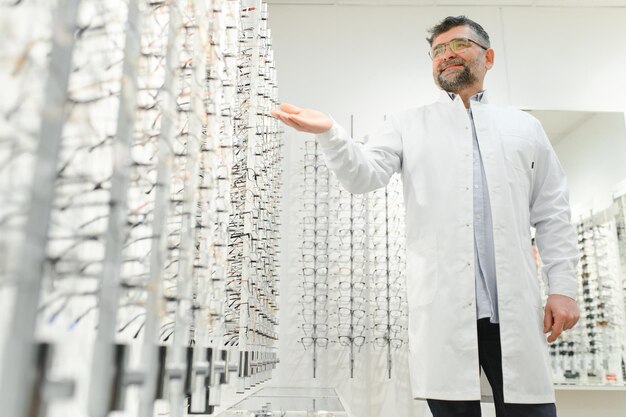 Portrait of a handsome ophthalmologist in front of the showcase with eyeglasses in the hospital