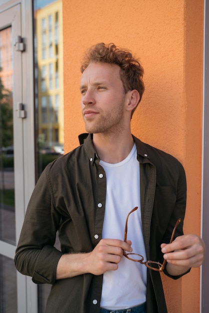 Photo portrait of handsome pensive man holding eyeglasses looking away on the street