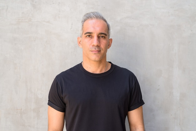 Portrait of handsome Persian man with gray hair against concrete wall outdoors