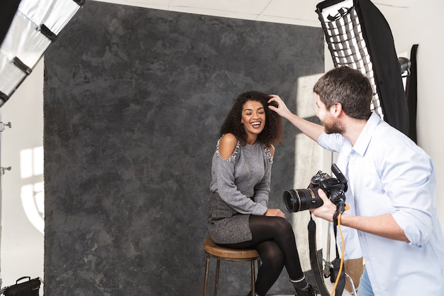 Portrait of handsome photographer man shooting young female model with professional camera and softbox in studio