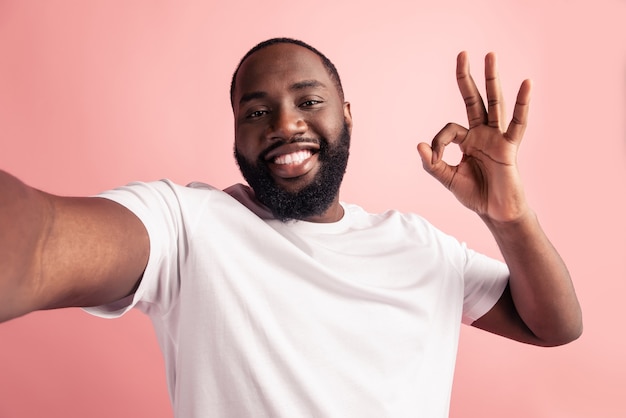 Portrait of handsome positive man shoot selfie show okey sign white smile on pink wall