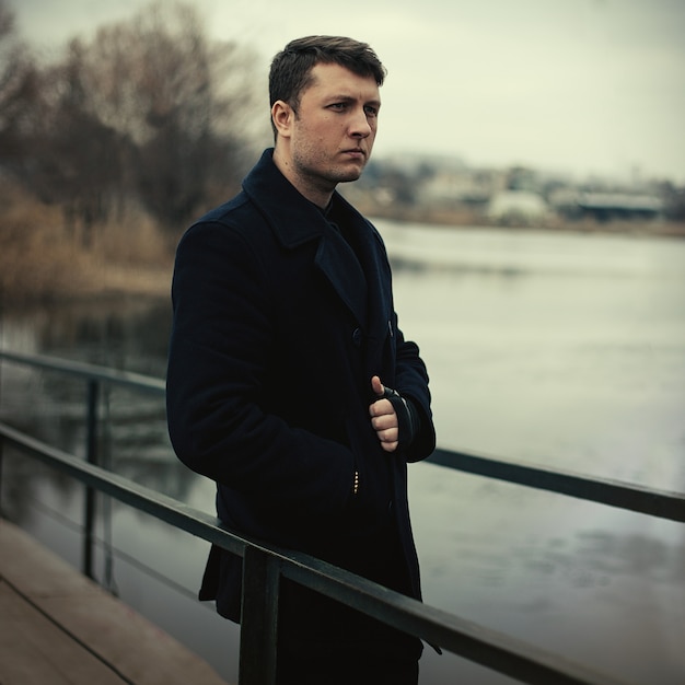 Portrait handsome serious man in coat outdoors in autumn park 