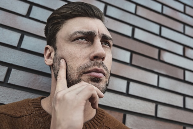 Ritratto di uomo serio bello pensare a qualcosa di isolato sul muro di mattoni marrone.