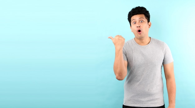 Portrait of handsome,Shock and surprise face of asian man Pointing finger  on empty space  isolated on blue  wall.